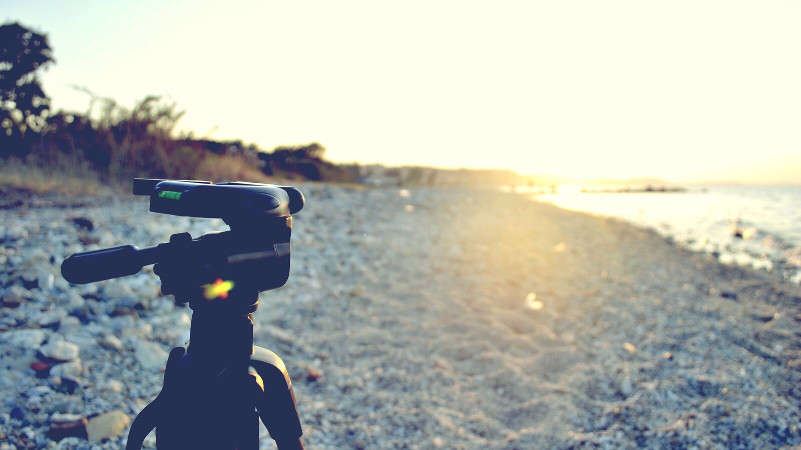 A camcorder on a tripod on a pebble beach at sunset