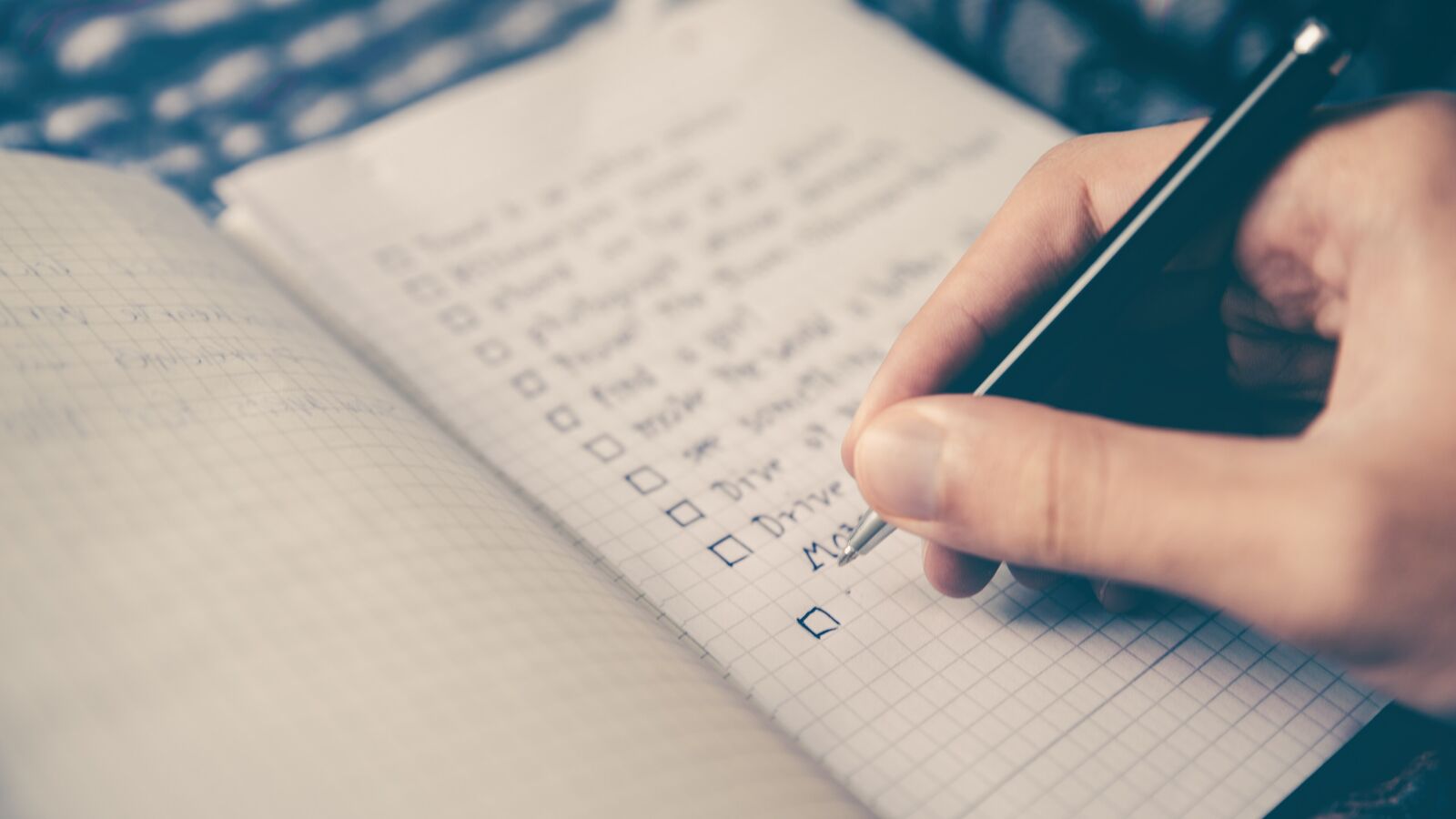 Eine Hand hakt mit einem Stift eine Checkliste in einem Notizbuch ab