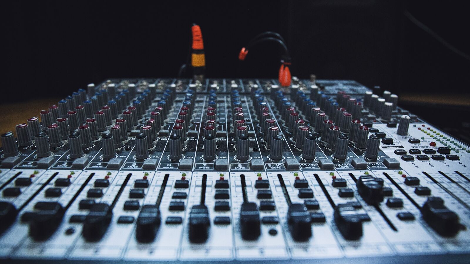 A mixing desk with many channel strips and knobs in bluish light