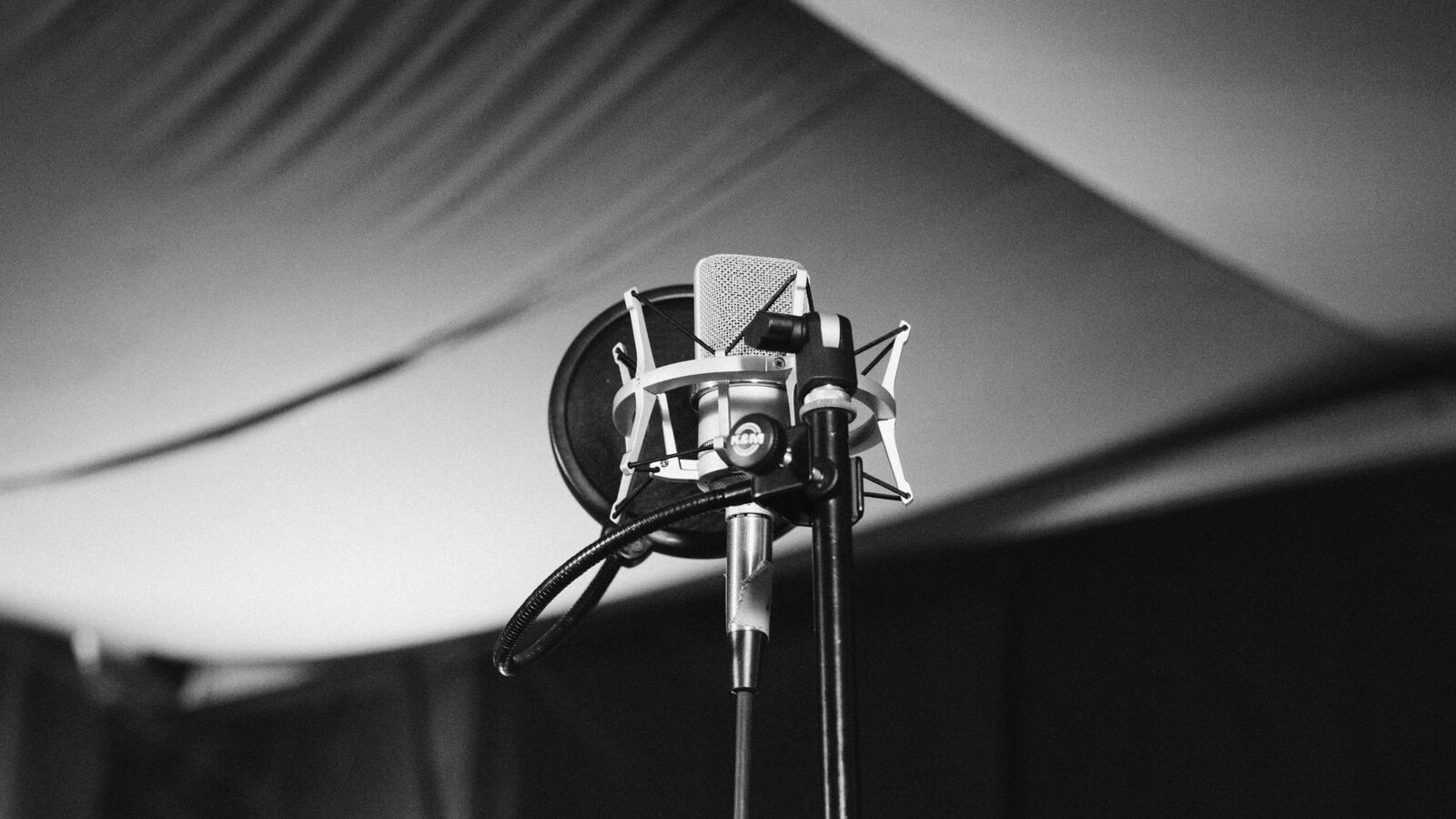 A condenser microphone with a pop filter on a stand in a dark recording room
